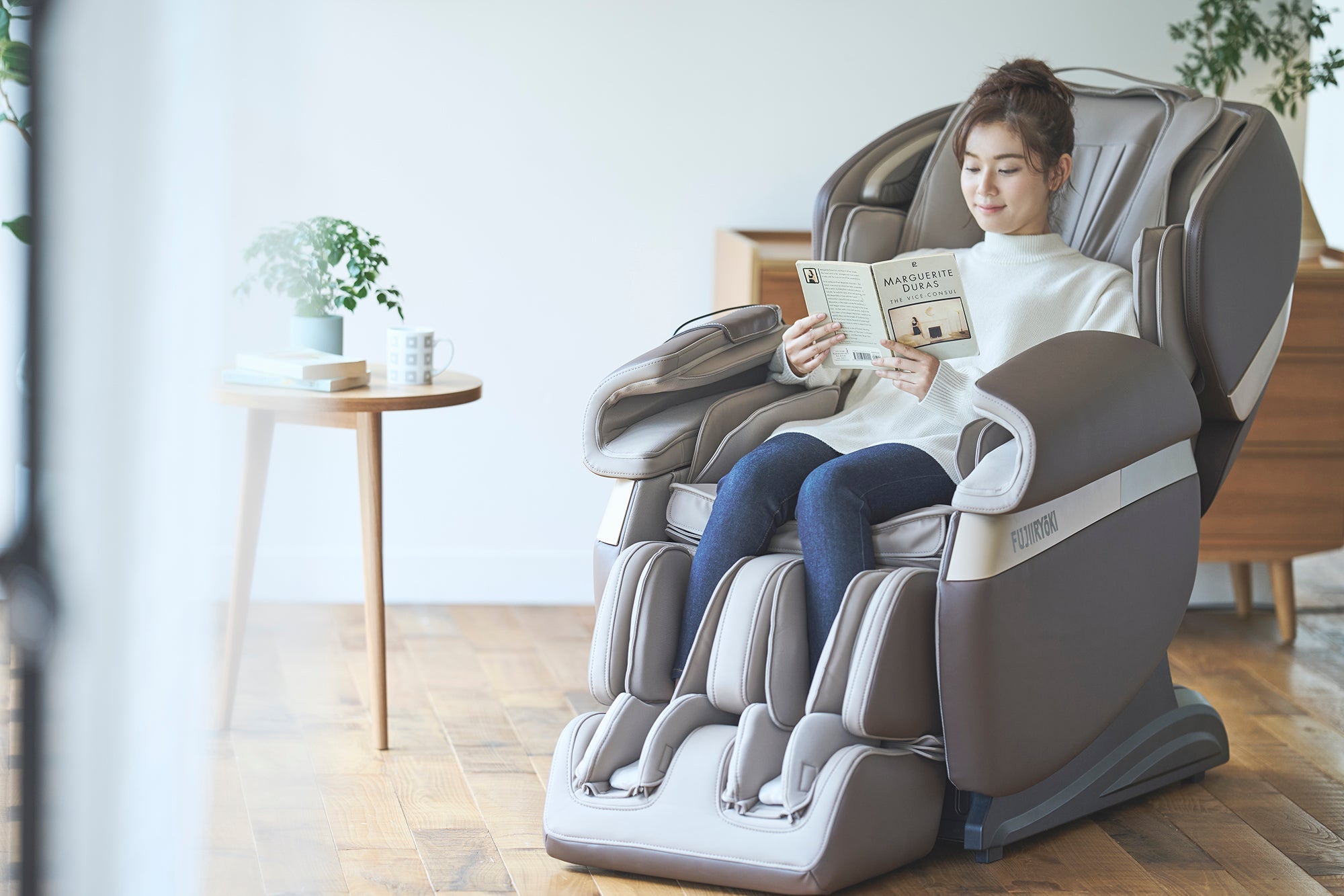 Woman reads a book in a massage chair next to a side table