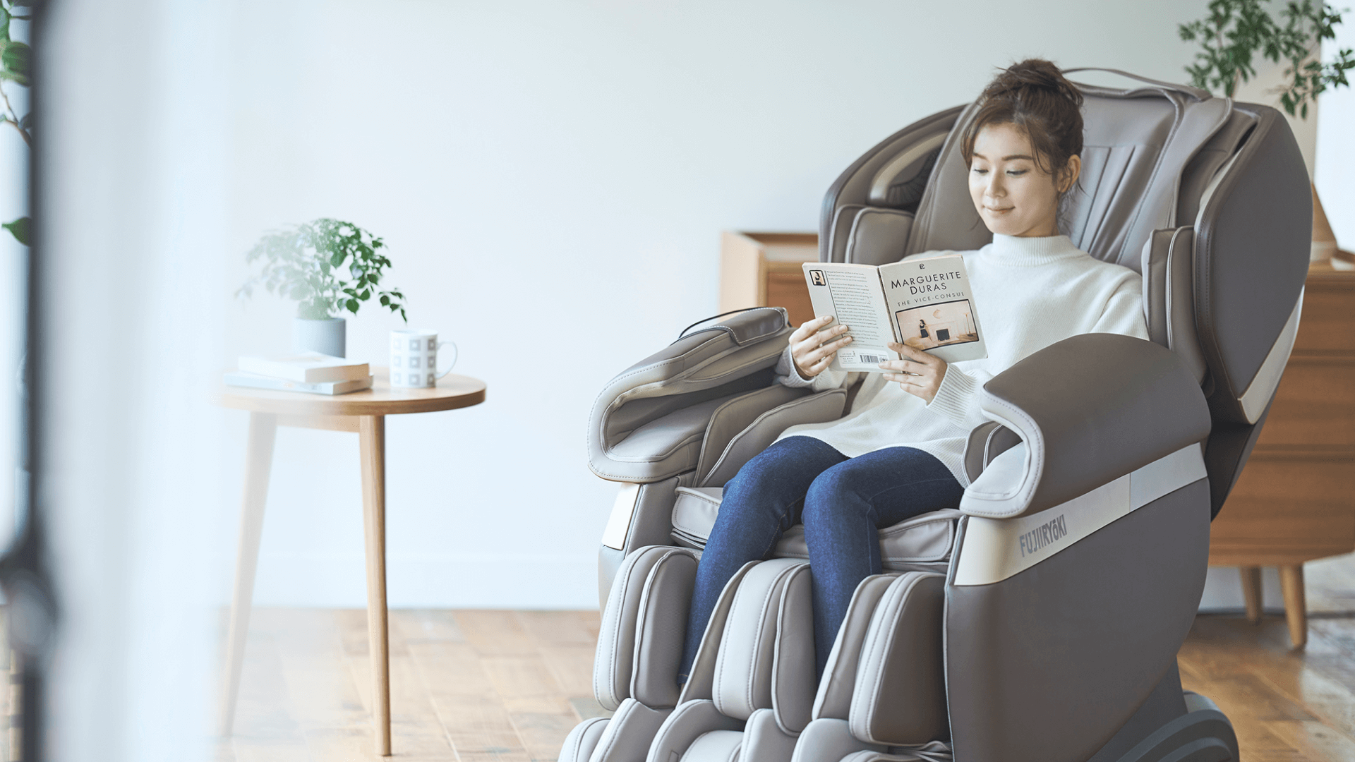 Woman reads a book while sitting in a massage chair by a side table