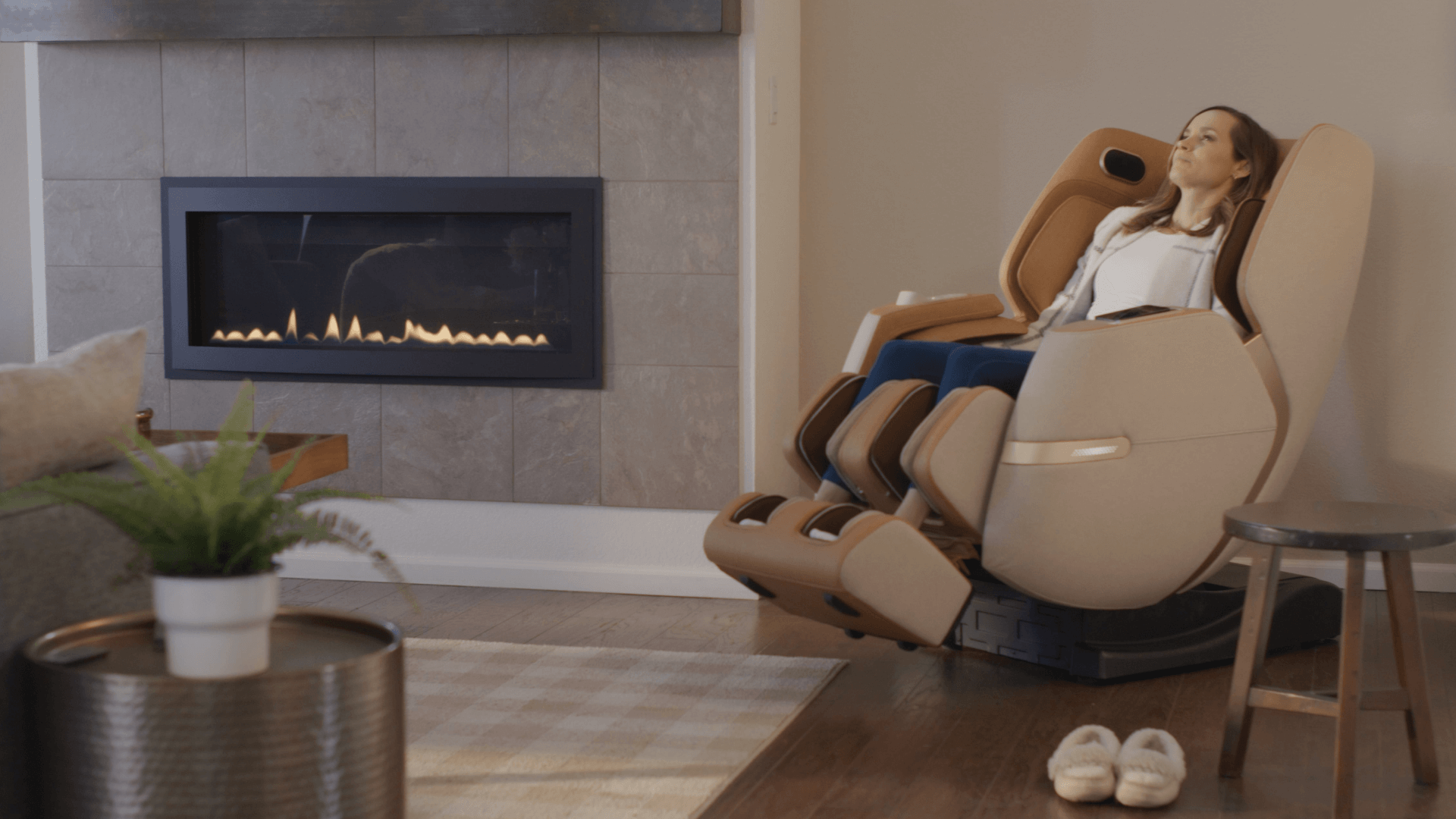Woman rests in a massage chair in a room with a modern fireplace